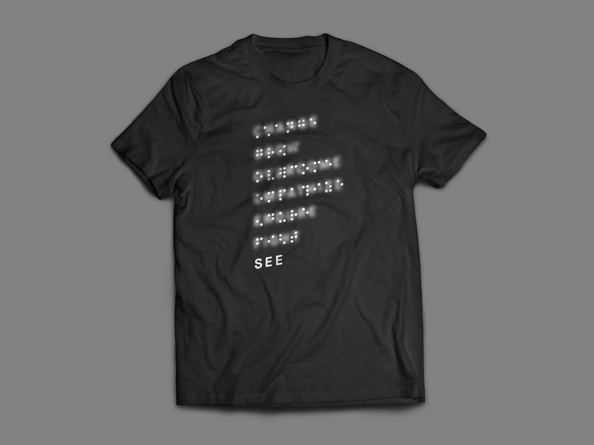 Black T-shirt printed with blurred braille words resolving to SEE